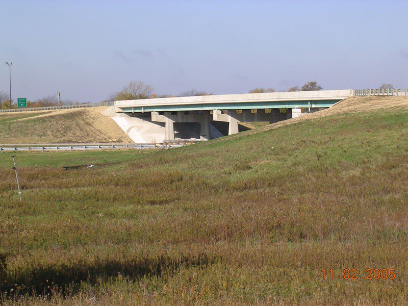 A highway with a bridge over it and grass in the foreground.