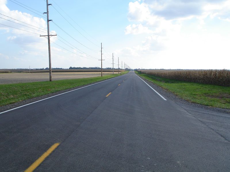 A road with power lines and grass on the side.
