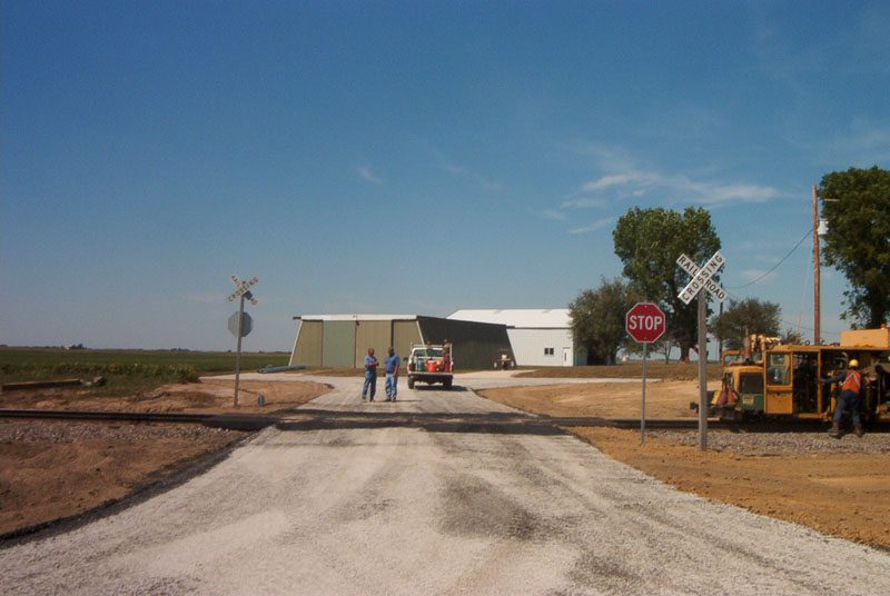 Two people standing on a dirt road near a train station.