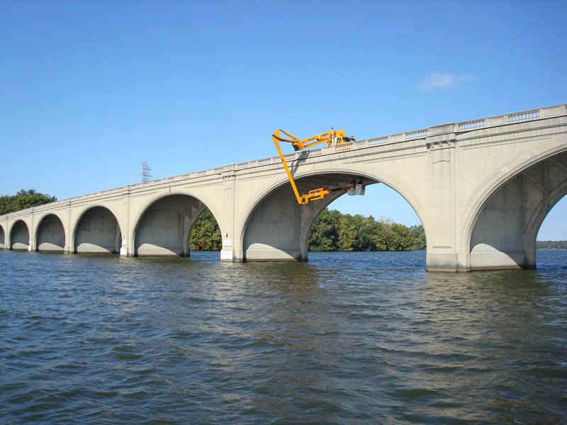 A bridge with two cranes on it and water in the background.