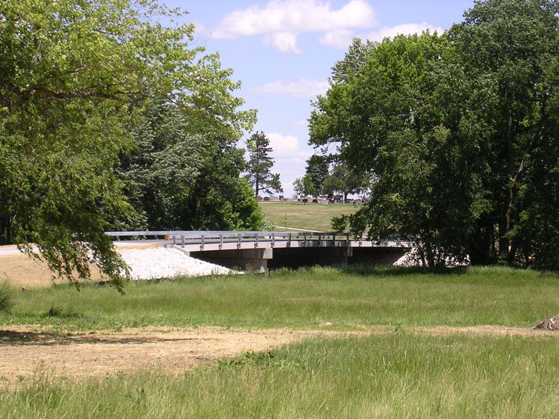 A bridge over a river in the middle of a field.
