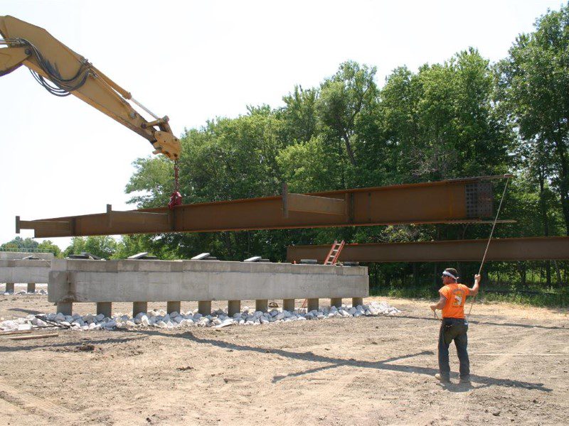 A man in an orange shirt is holding onto a crane